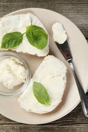 Photo of Delicious sandwiches with cream cheese and basil leaves on wooden table, top view