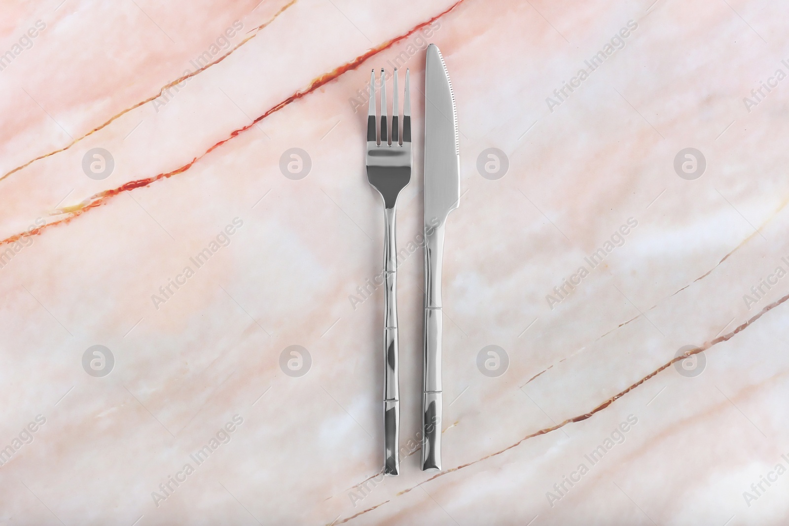 Photo of Shiny fork and knife on pink marble table, flat lay