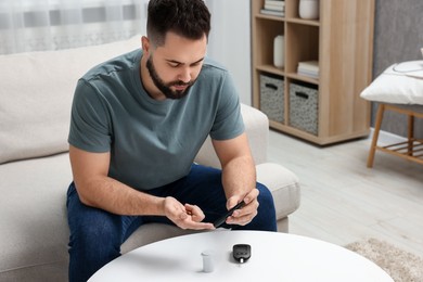 Photo of Diabetes test. Man checking blood sugar level with lancet pen at table indoors