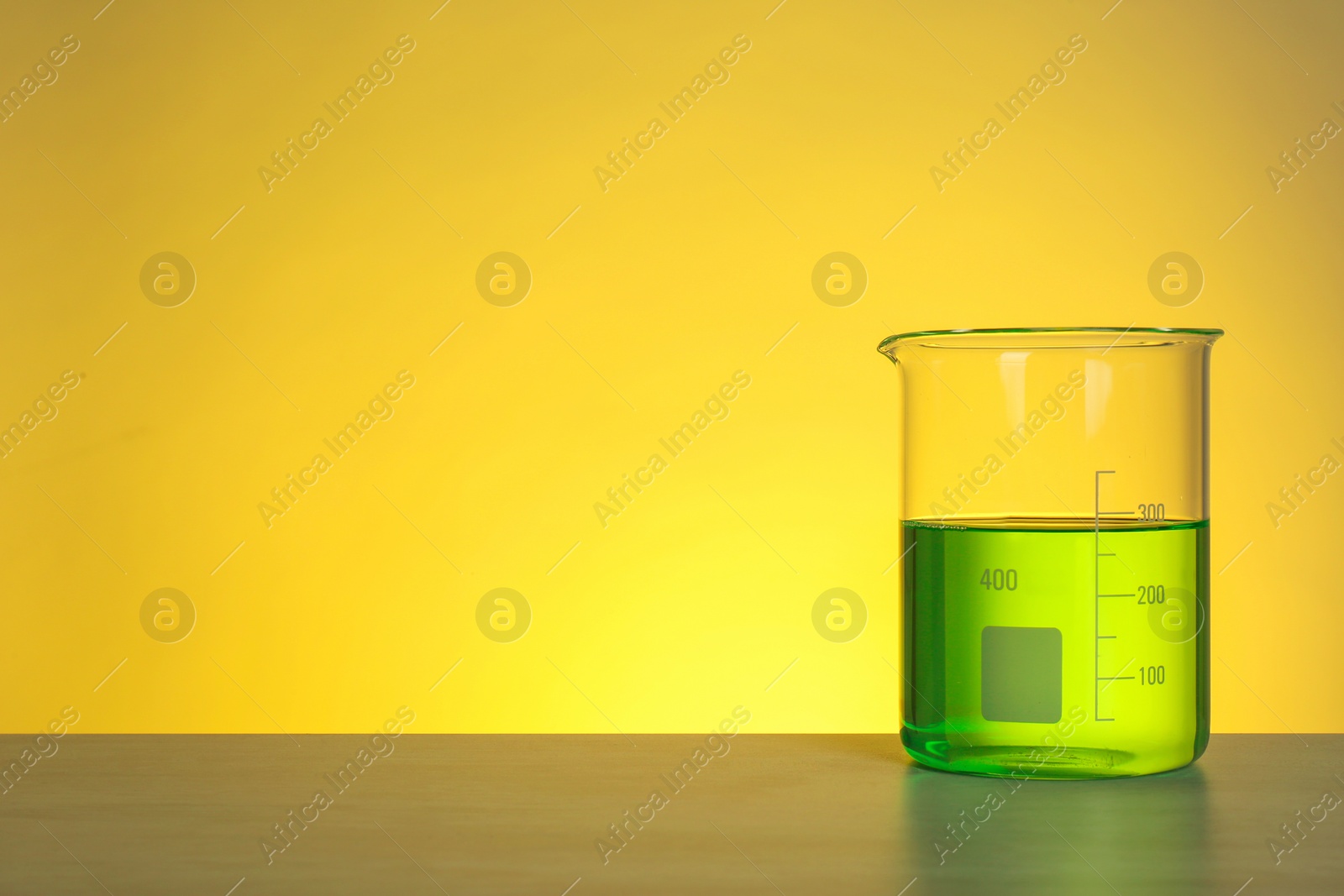 Photo of Beaker with liquid on table against color background. Chemistry laboratory glassware