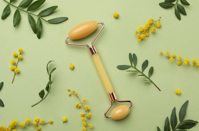 Natural face roller and flowers on green background, flat lay