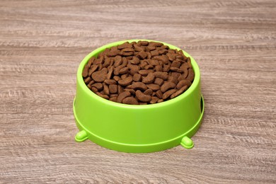 Photo of Dry food in green pet bowl on wooden surface