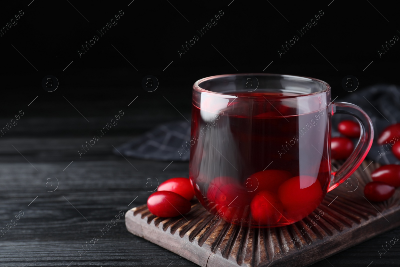 Photo of Glass cup of fresh dogwood tea with berries on black wooden table. Space for text