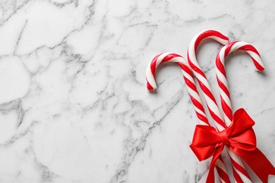 Photo of Candy canes with bow on white marble background, top view with space for text. Traditional Christmas treat