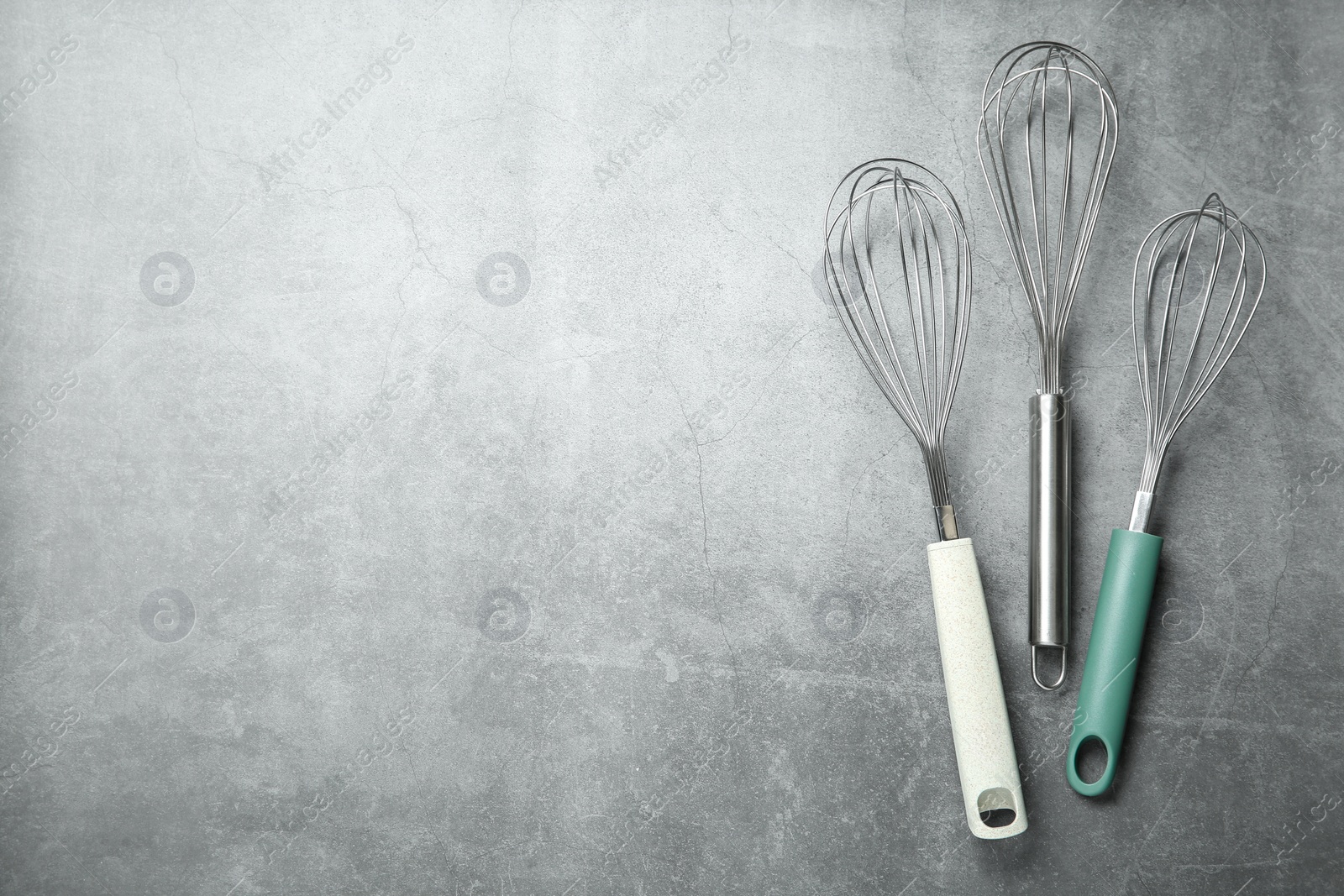 Photo of Metal whisks on gray table, top view. Space for text