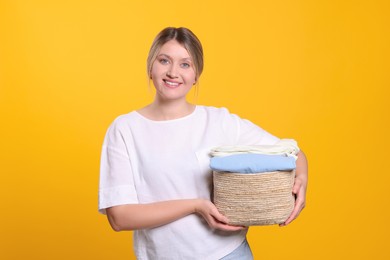 Happy woman with basket full of laundry on orange background