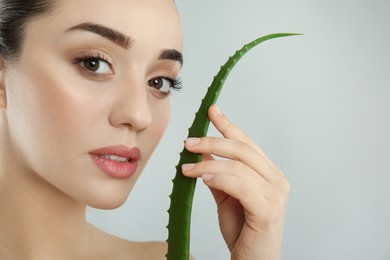 Photo of Young woman with aloe vera leaf on light grey background, closeup