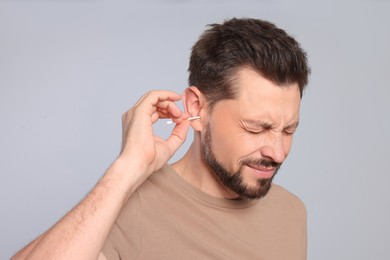 Man cleaning ears and suffering from pain on grey background