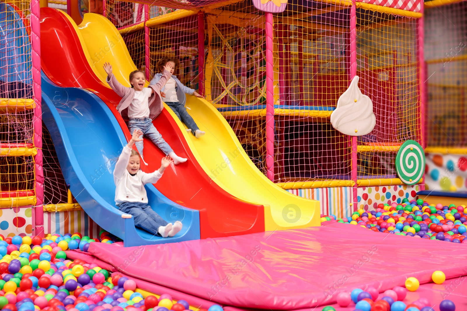 Photo of Happy kids playing in play room with slides, mats and ball pit