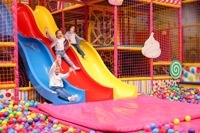 Photo of Happy kids playing in play room with slides, mats and ball pit