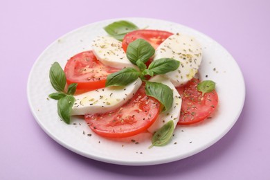 Photo of Plate of delicious Caprese salad with herbs on violet table, closeup