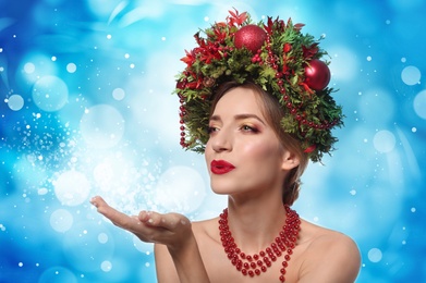 Beautiful young woman with Christmas wreath blowing kiss on blue background
