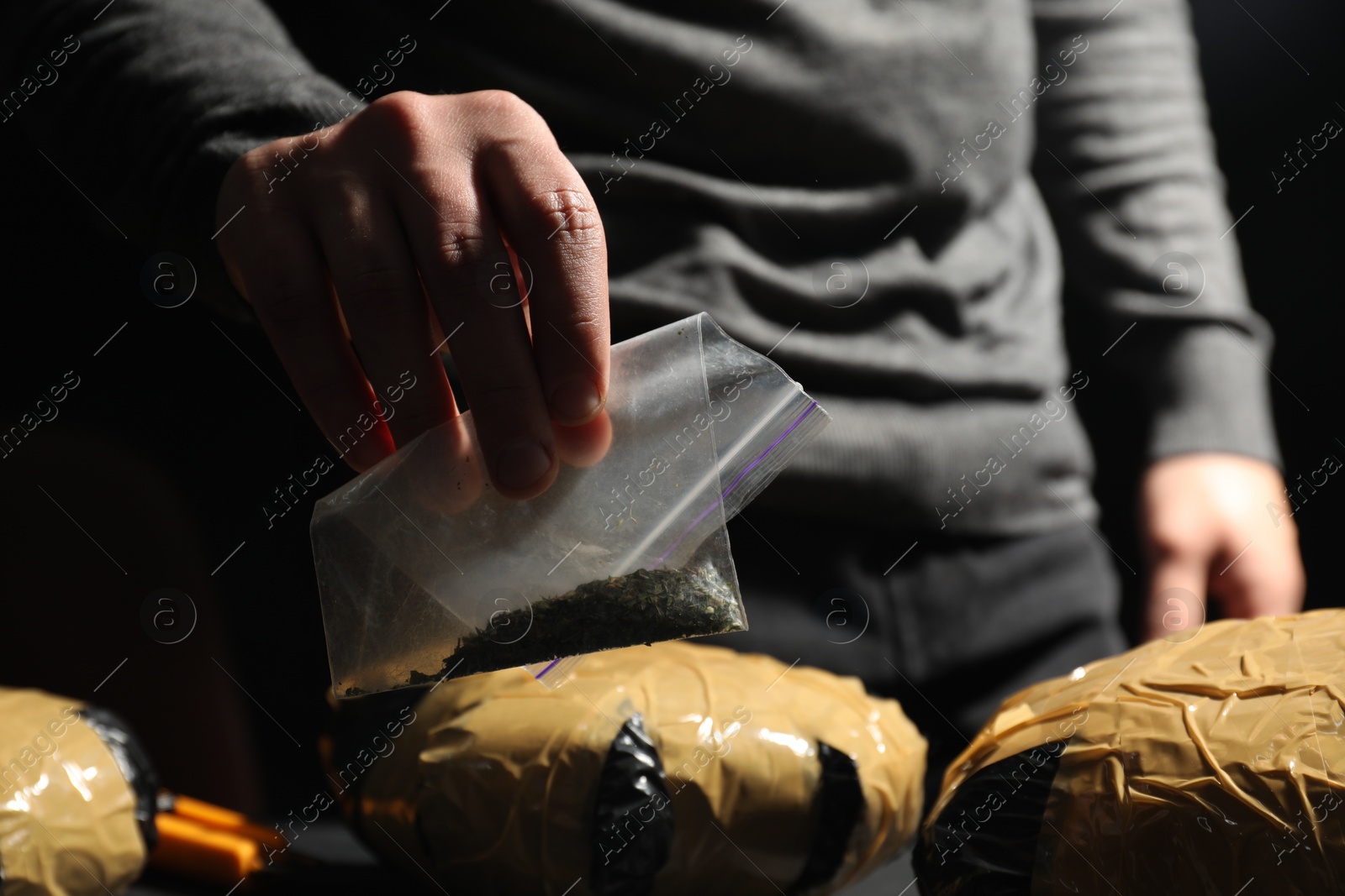 Photo of Smuggling and drug trafficking. Man giving plastic bag with hemp on dark background, closeup