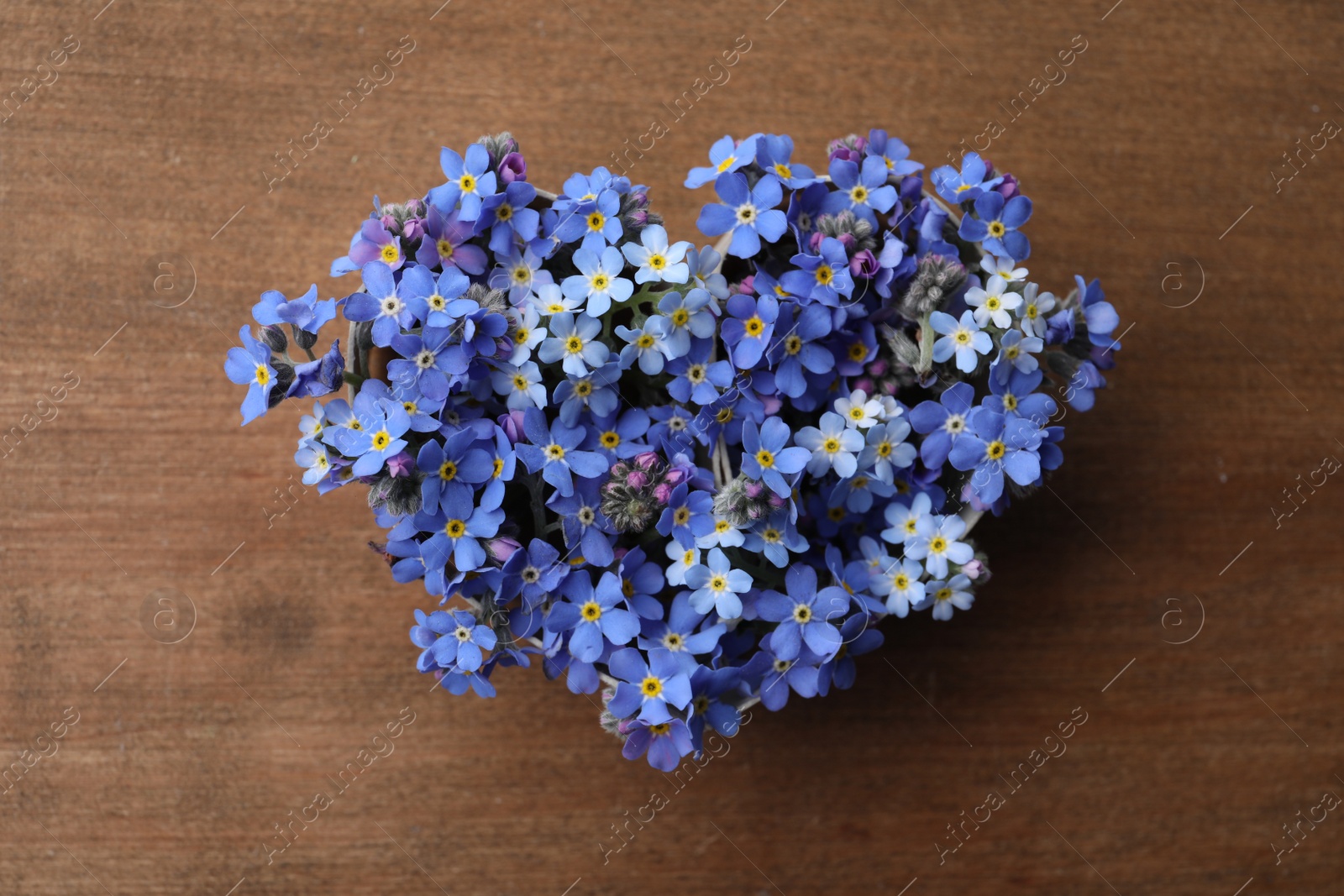 Photo of Heart of beautiful blue forget-me-not flowers on wooden table, top view