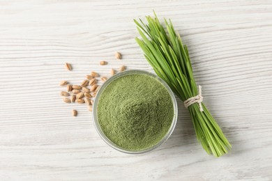 Wheat grass powder in bowl, seeds and fresh sprouts on white wooden table, flat lay