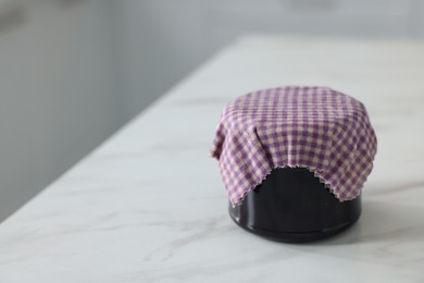 Photo of Jar of jam covered with beeswax food wrap on white table, closeup. Space for text