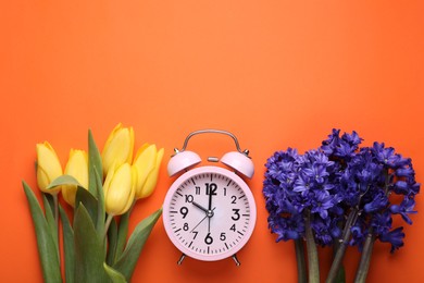 Photo of Pink alarm clock and beautiful flowers on orange background, flat lay. Spring time