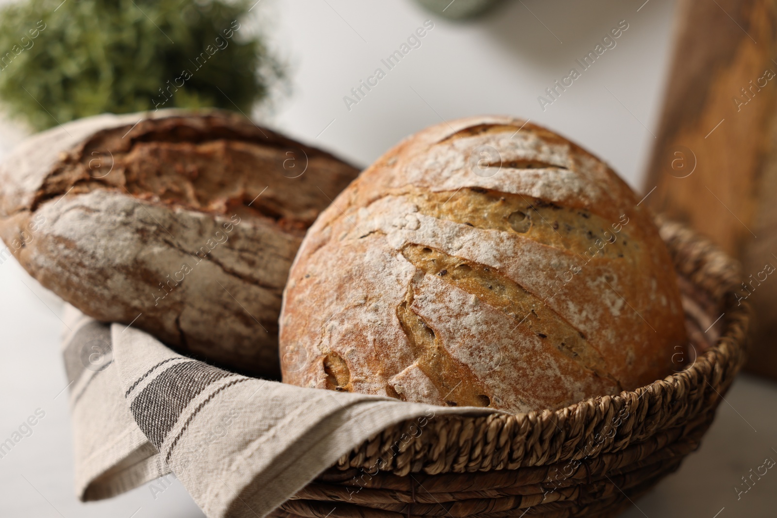 Photo of Wicker bread basket with freshly baked loaves on table in kitchen, closeup