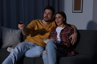 Photo of Couple watching TV at home in evening. Man changing channels with remote control