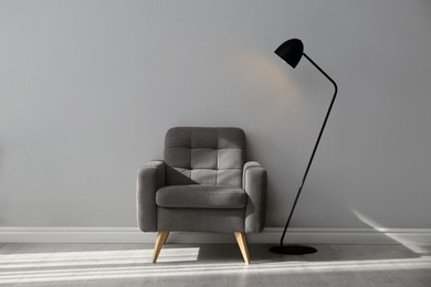 Stylish armchair and lamp near grey wall. Interior design