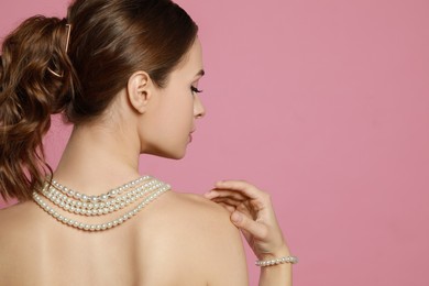 Photo of Young woman wearing elegant pearl jewelry on pink background, back view. Space for text
