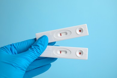 Photo of Doctor holding two disposable express tests for hepatitis on light blue background, closeup