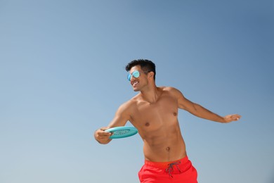 Happy man throwing flying disk against blue sky on sunny day