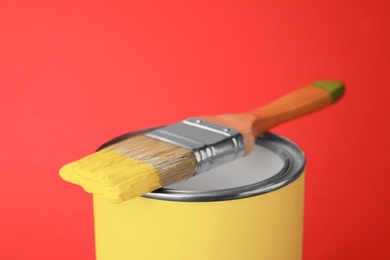 Photo of Can of yellow paint with brush on red background