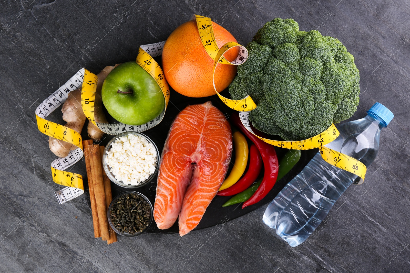 Photo of Metabolism. Different food products and measuring tape on grey table, flat lay