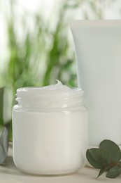 Photo of Different hand care cosmetic products and eucalyptus branches on white wooden table, closeup