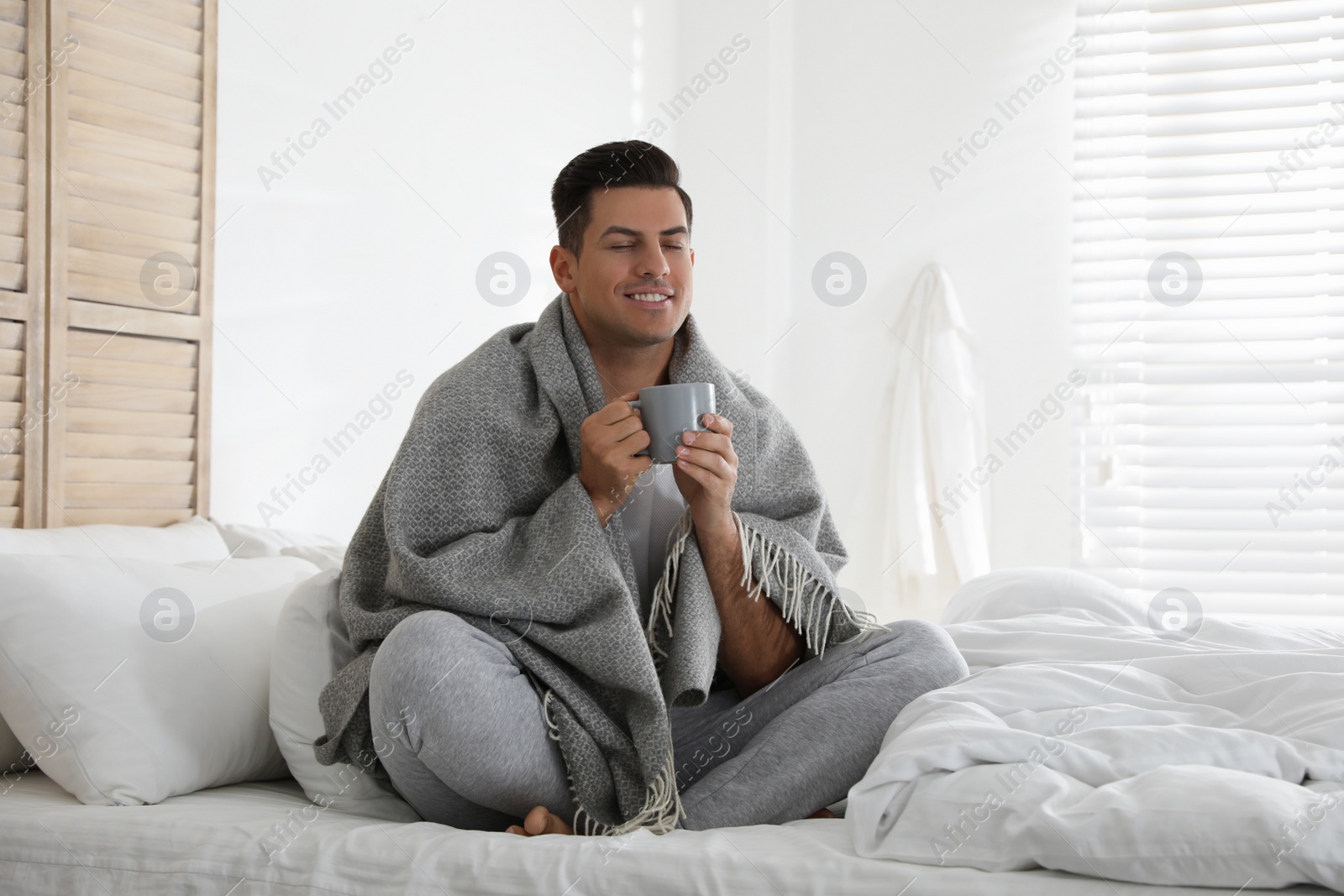 Photo of Man covered with warm grey plaid enjoying hot morning drink in bedroom