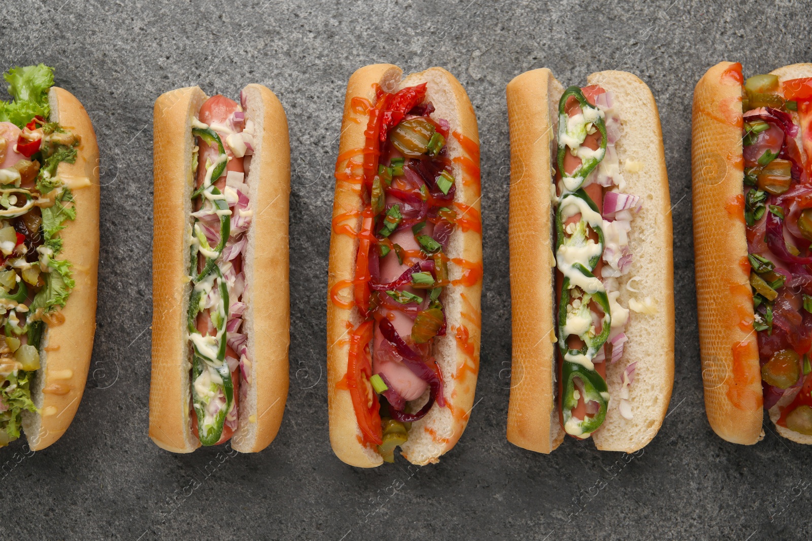 Photo of Delicious hot dogs with different toppings on grey table, flat lay