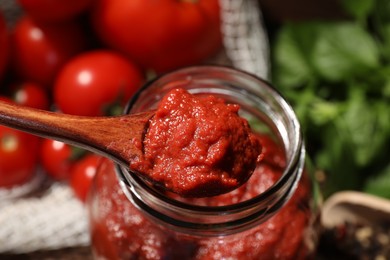 Photo of Taking tasty tomato sauce with wooden spoon from jar on table, closeup