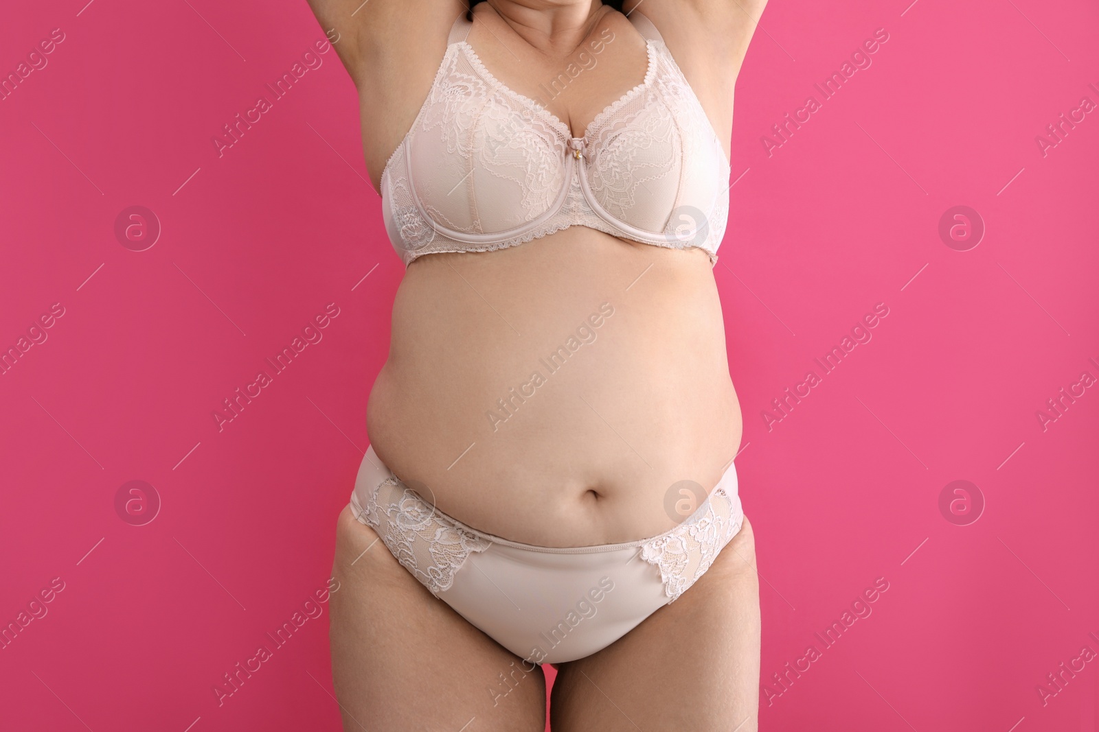 Photo of Overweight woman in beige underwear on pink background, closeup. Plus-size model