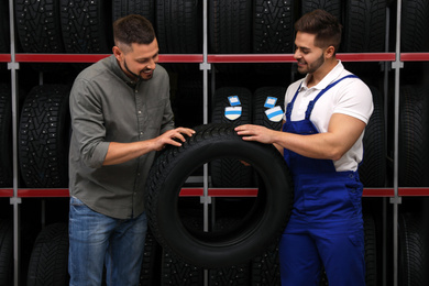 Mechanic helping client to choose car tire in auto store