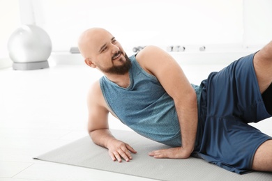 Photo of Overweight man doing exercise on mat in gym