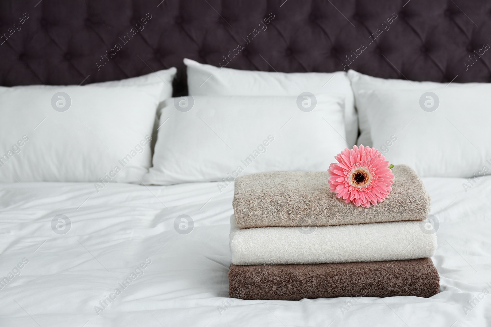 Photo of Stack of clean towels and beautiful gerbera flower on bed. Space for text