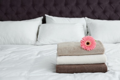 Photo of Stack of clean towels and beautiful gerbera flower on bed. Space for text