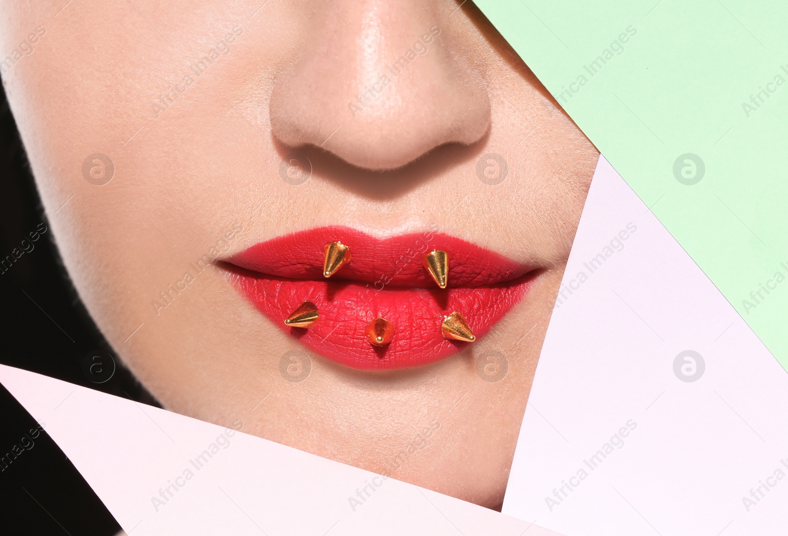 Photo of Beautiful young model with decorative spikes on lips and paper against black background