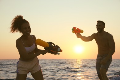 Photo of Couple with water guns having fun on beach at sunset