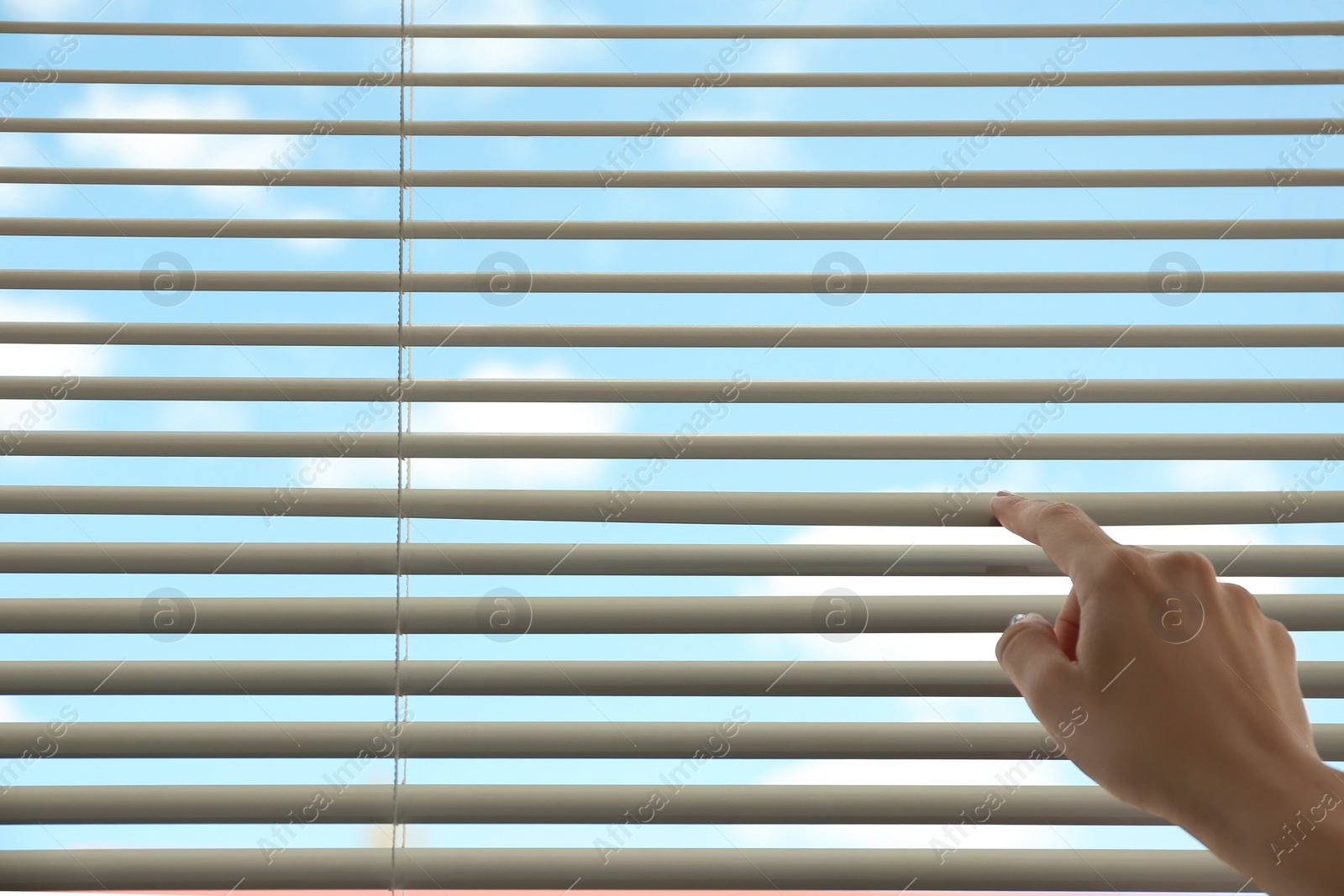 Photo of Woman opening horizontal window blinds at home, closeup. Space for text