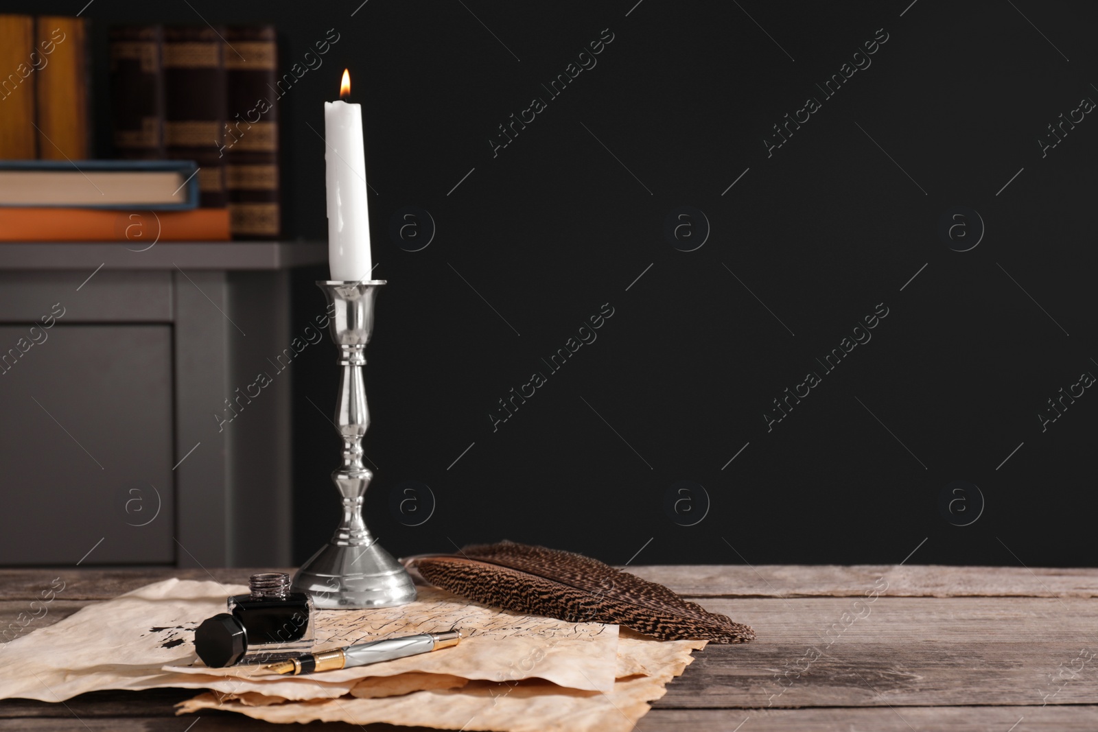 Photo of Inkwell, feather, fountain pen, candlestick and vintage parchment with ink stains on wooden table indoors. Space for text