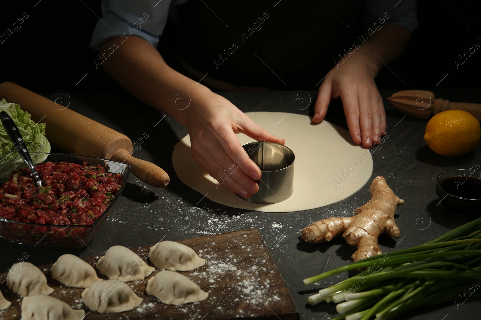 Photo of Woman cutting dough for gyoza at grey table, closeup