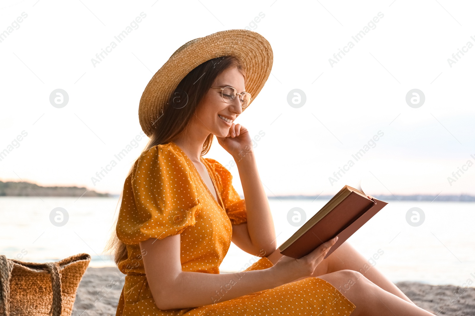 Photo of Young woman reading book on sandy beach near sea