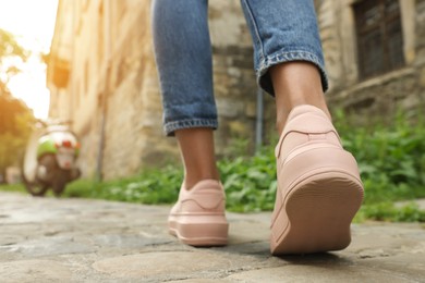 Woman in stylish sneakers walking on city street, closeup