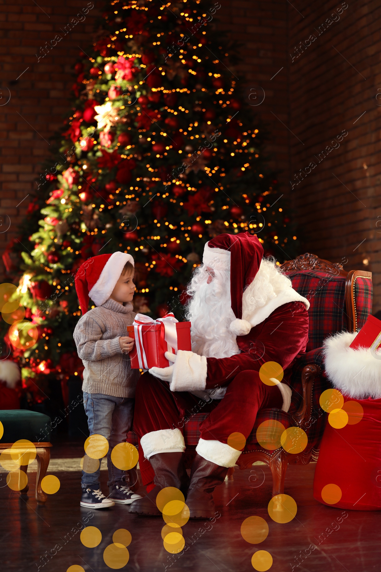 Photo of Santa Claus giving present to little boy near Christmas tree indoors