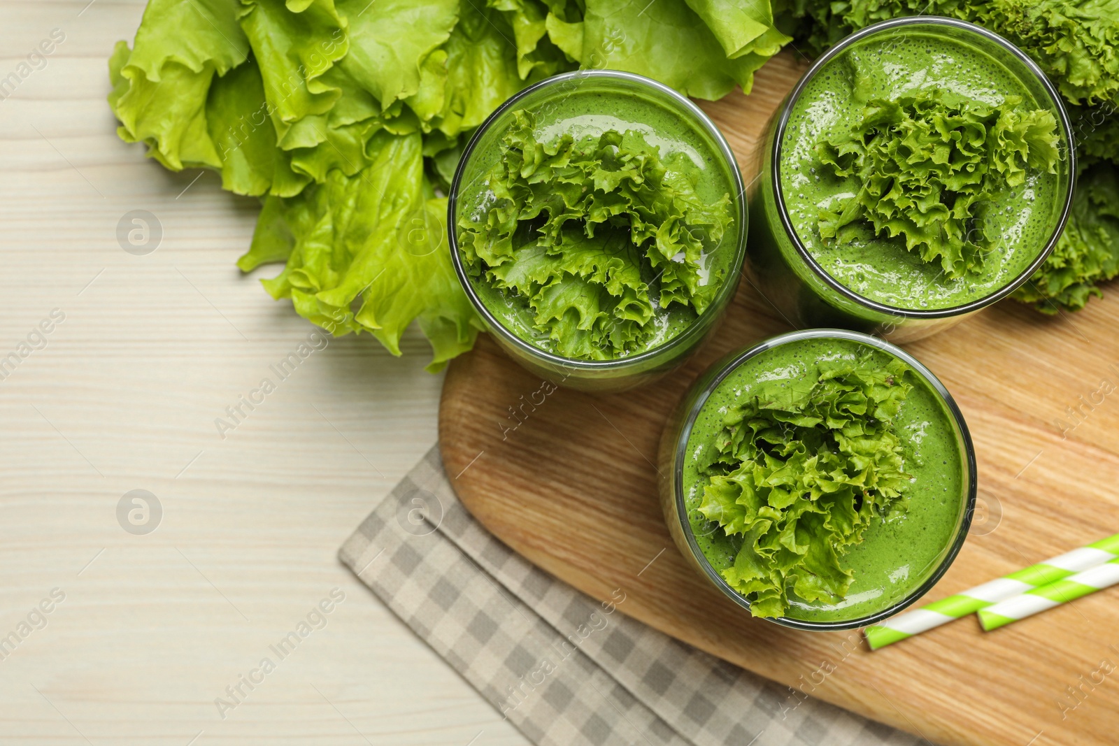 Photo of Green smoothie of lettuce leaves in glasses on white wooden table, flat lay. Space for text