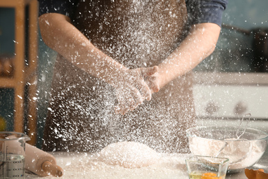 Image of Man sprinkling flour over dough on table in kitchen, closeup