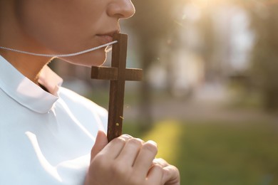 Photo of Young nun with Christian cross outdoors on sunny day, closeup. Space for text