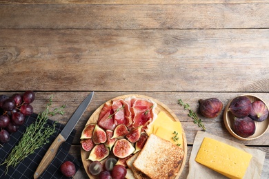 Photo of Delicious ripe figs, prosciutto and cheese served on wooden table, flat lay. Space for text